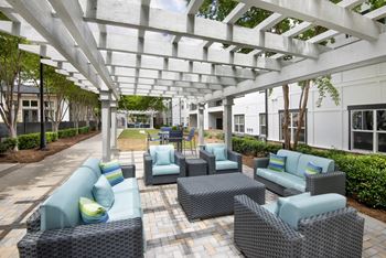 A patio with a white pergola and grey wicker furniture.